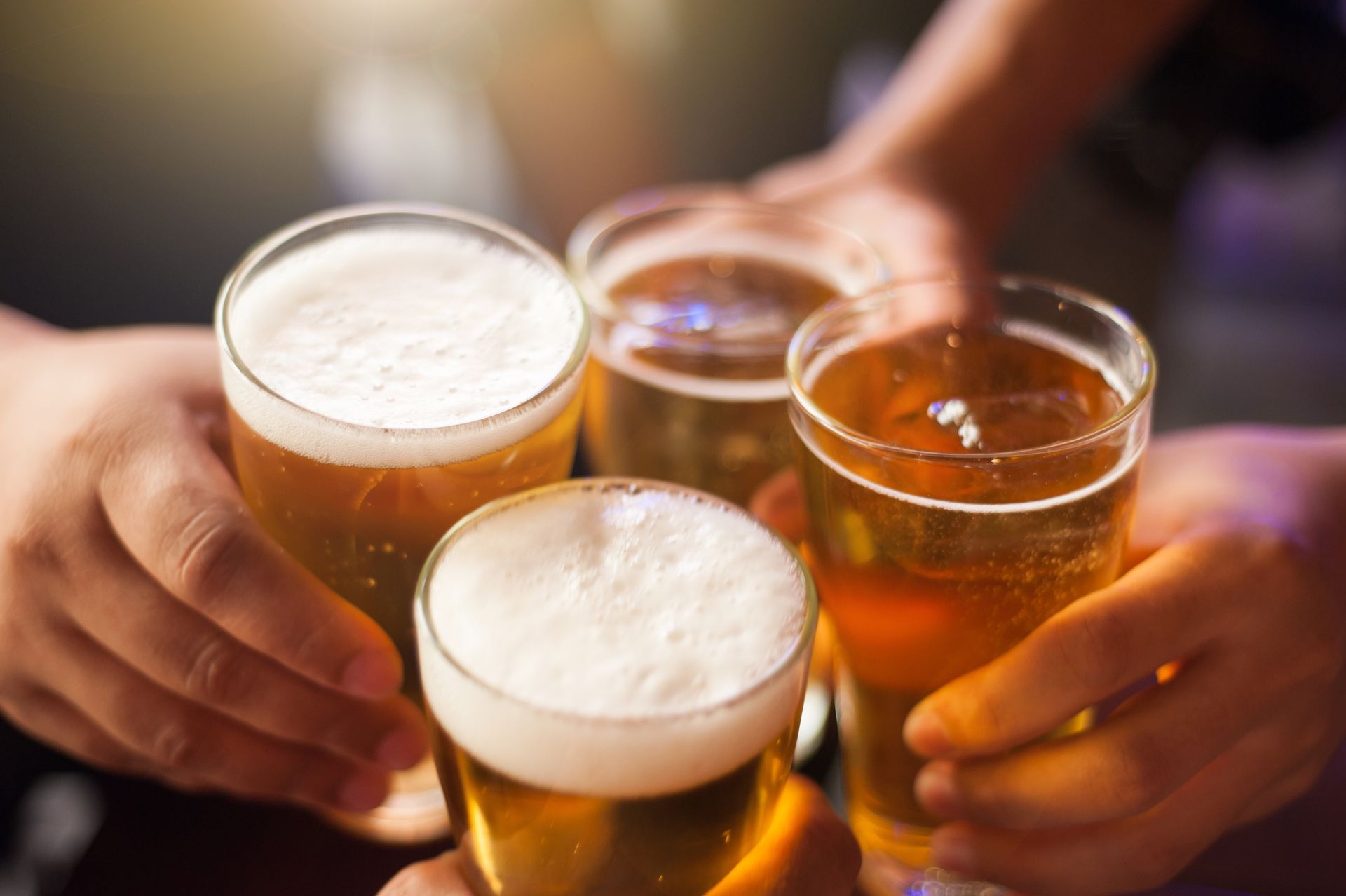 Hands clinking beer glasses at a bar, with foamy pints and amber drinks visible
