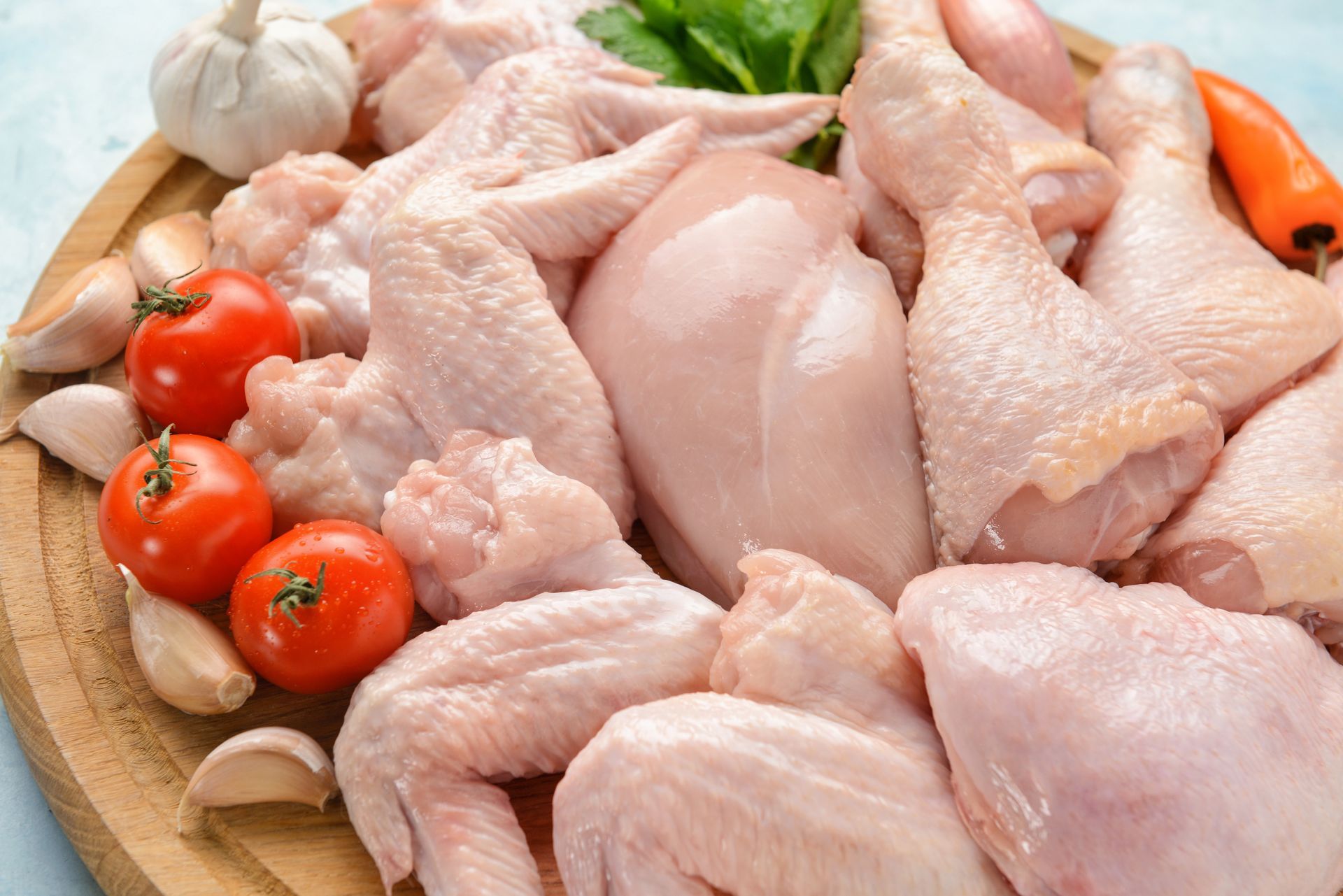 Raw chicken pieces with cherry tomatoes and garlic on a wooden cutting board