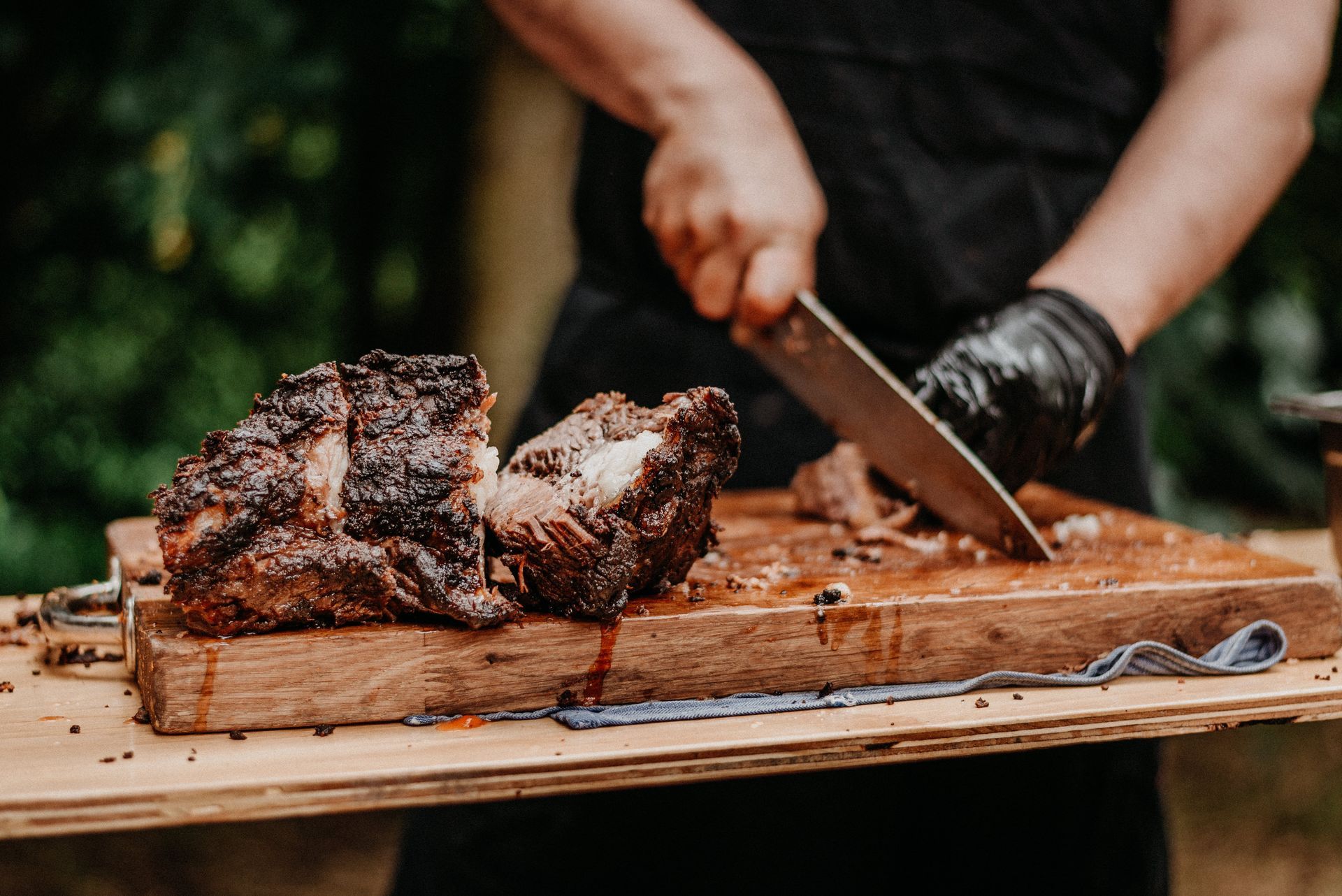 Person slicing grilled meat on a wooden board outdoors Person slicing grilled meat on a wooden board outdoors
