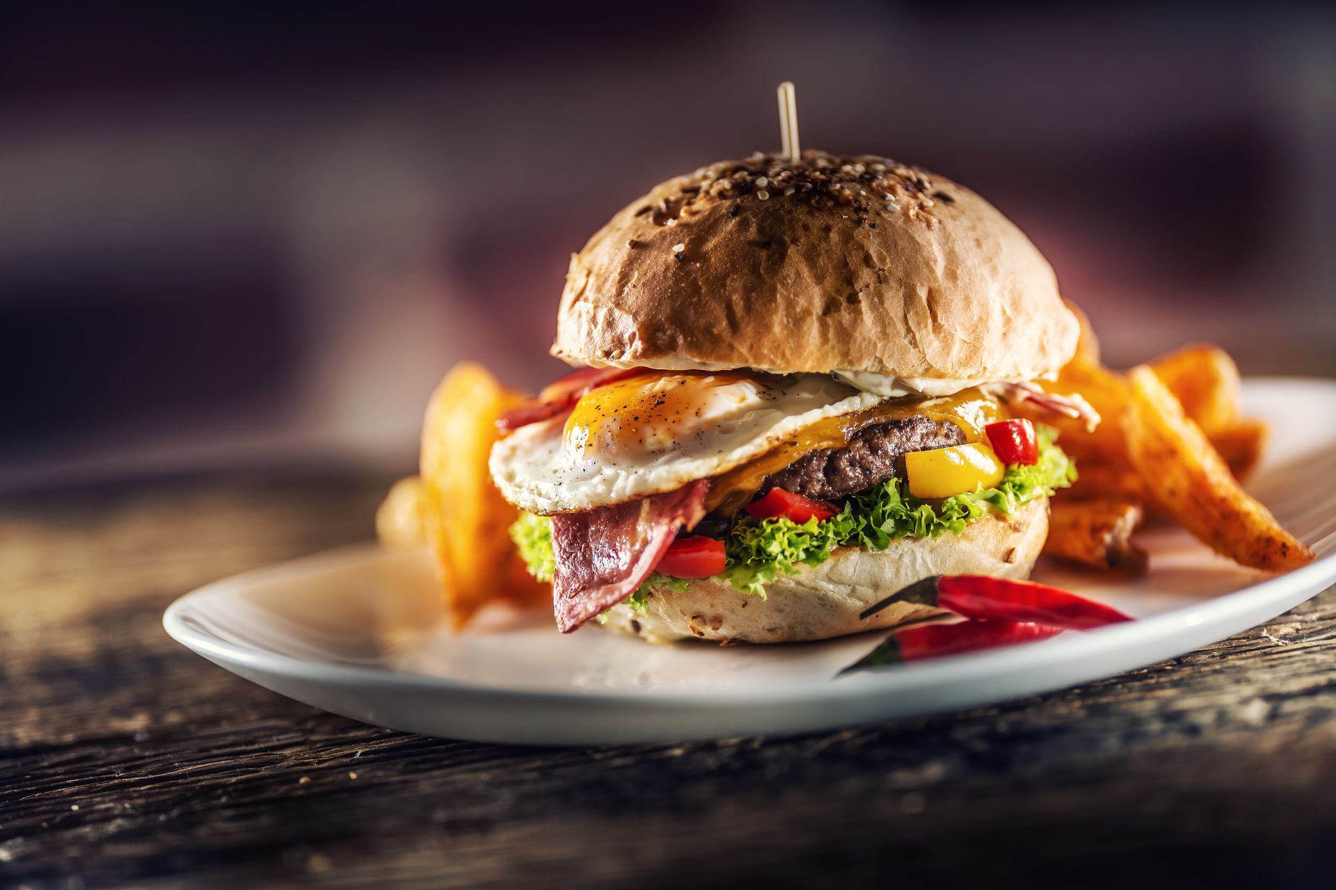 Burger with fries on a plate, topped with bacon and sauce, on a rustic table