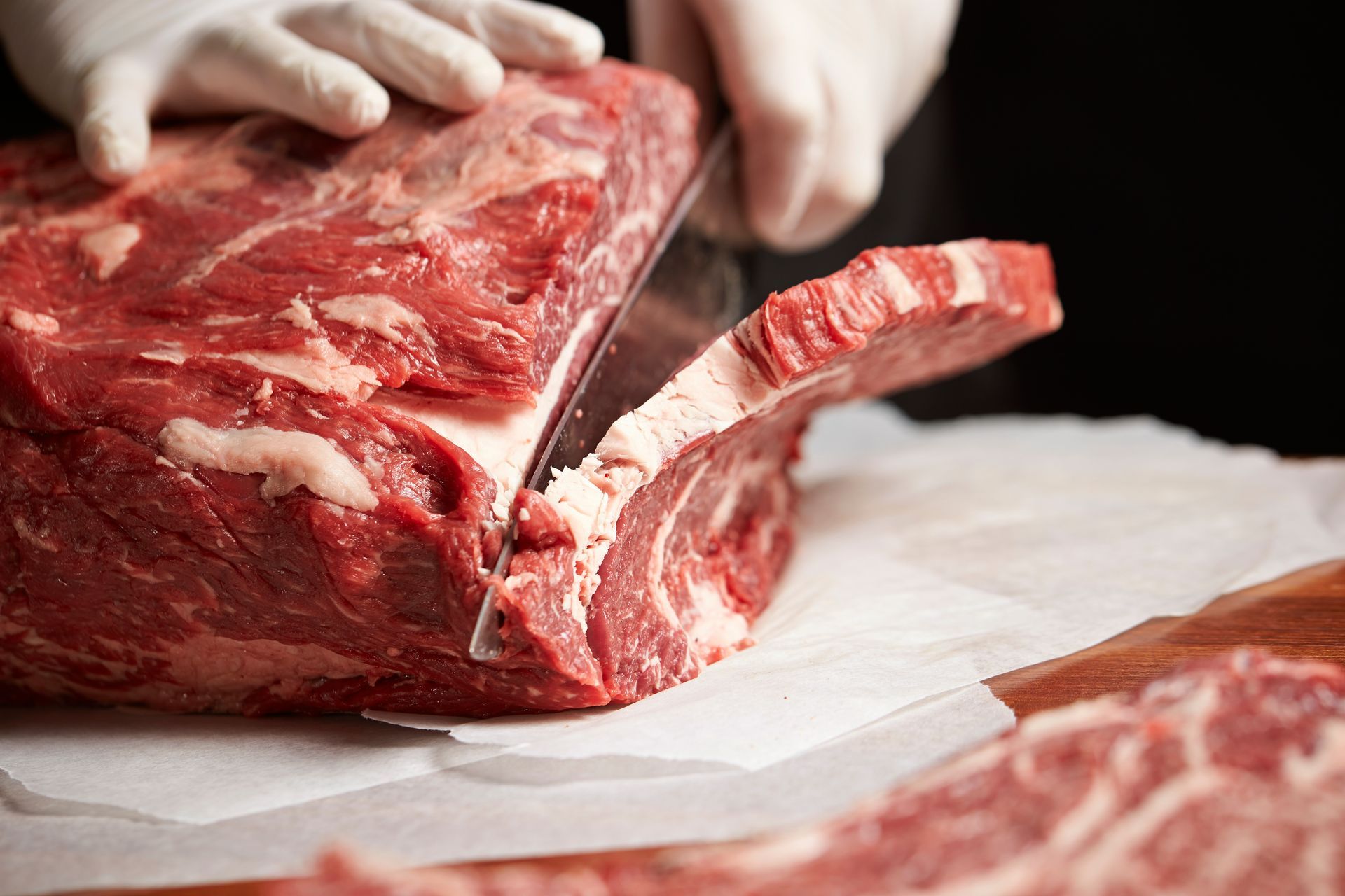 Hands slicing a raw red meat roast on a cutting board with a large knife