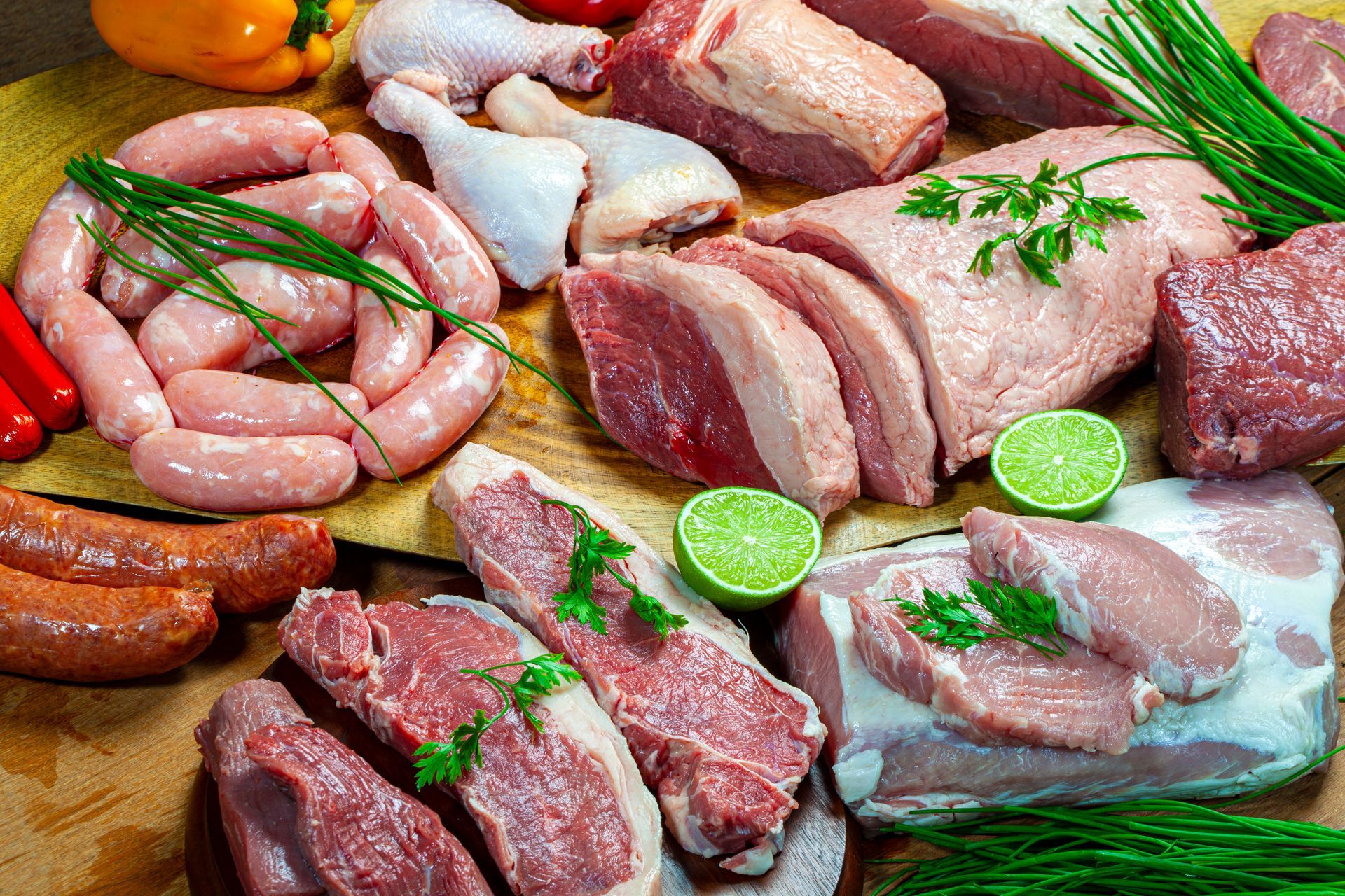 Assorted raw meats and sausages arranged on a wooden surface with herbs and lime slices
