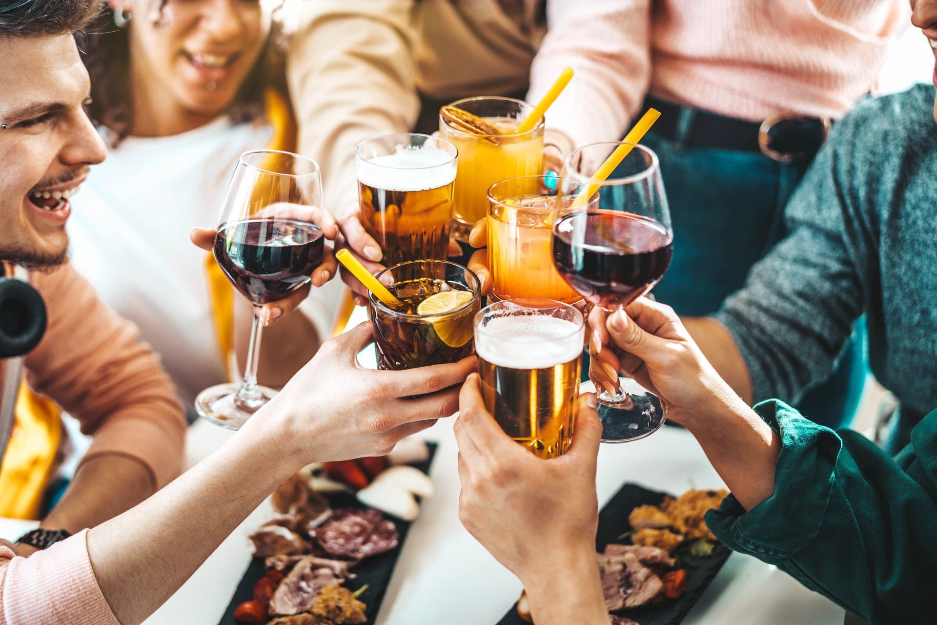 Friends clinking drinks around a table with beer, wine, and cocktails at a social gathering Friends clinking drinks around a table with beer, wine, and cocktails at a social gathering