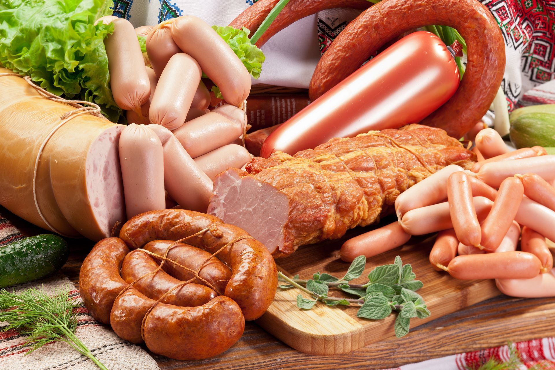 Assorted sausages, hot dogs, and cured meats arranged on a wooden board with lettuce and herbs Assorted sausages, hot dogs, and cured meats arranged on a wooden board with lettuce and herbs