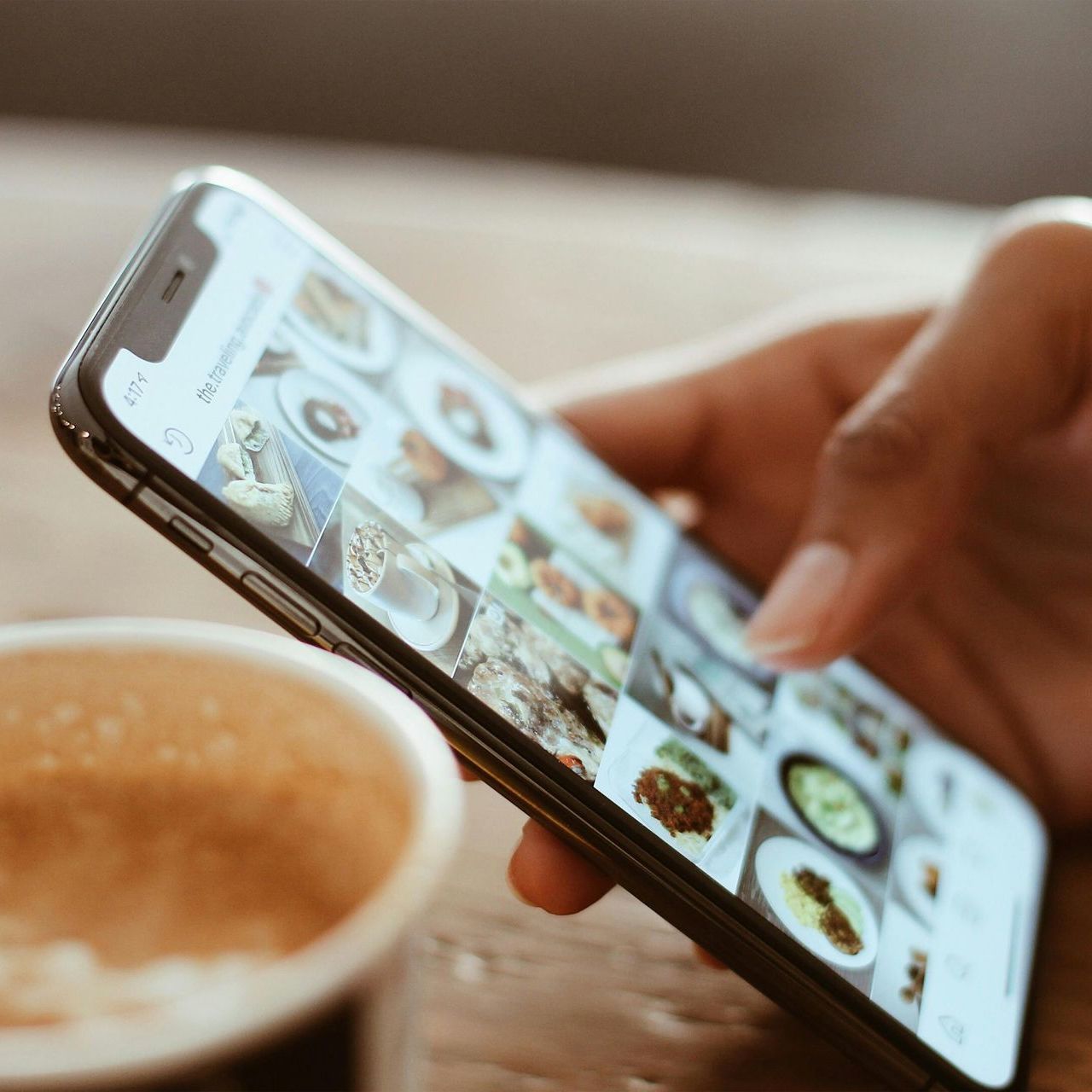 A person is holding a cell phone next to a cup of coffee