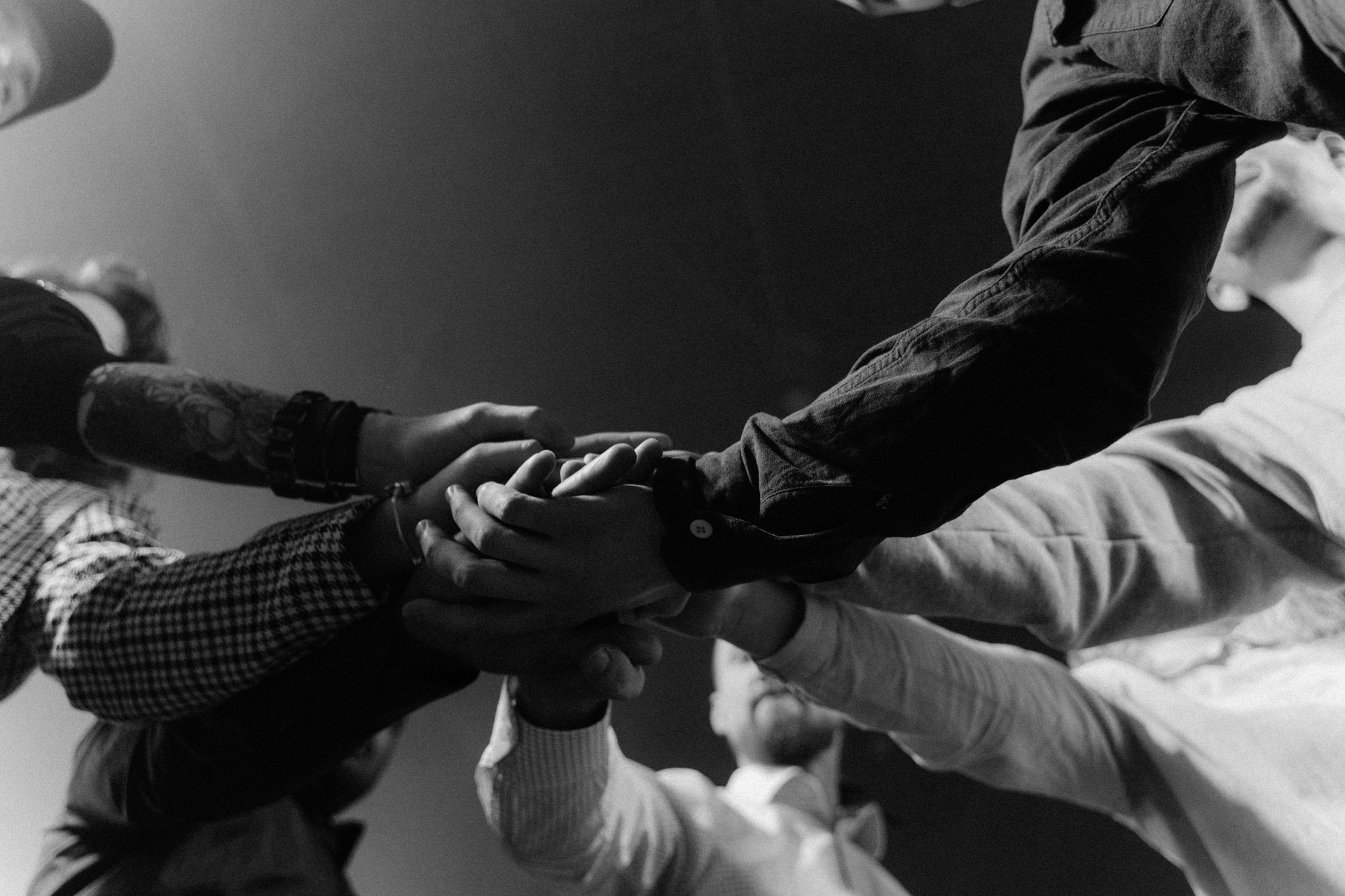 Hands clasped together in a circle, symbolizing teamwork and unity, black and white.