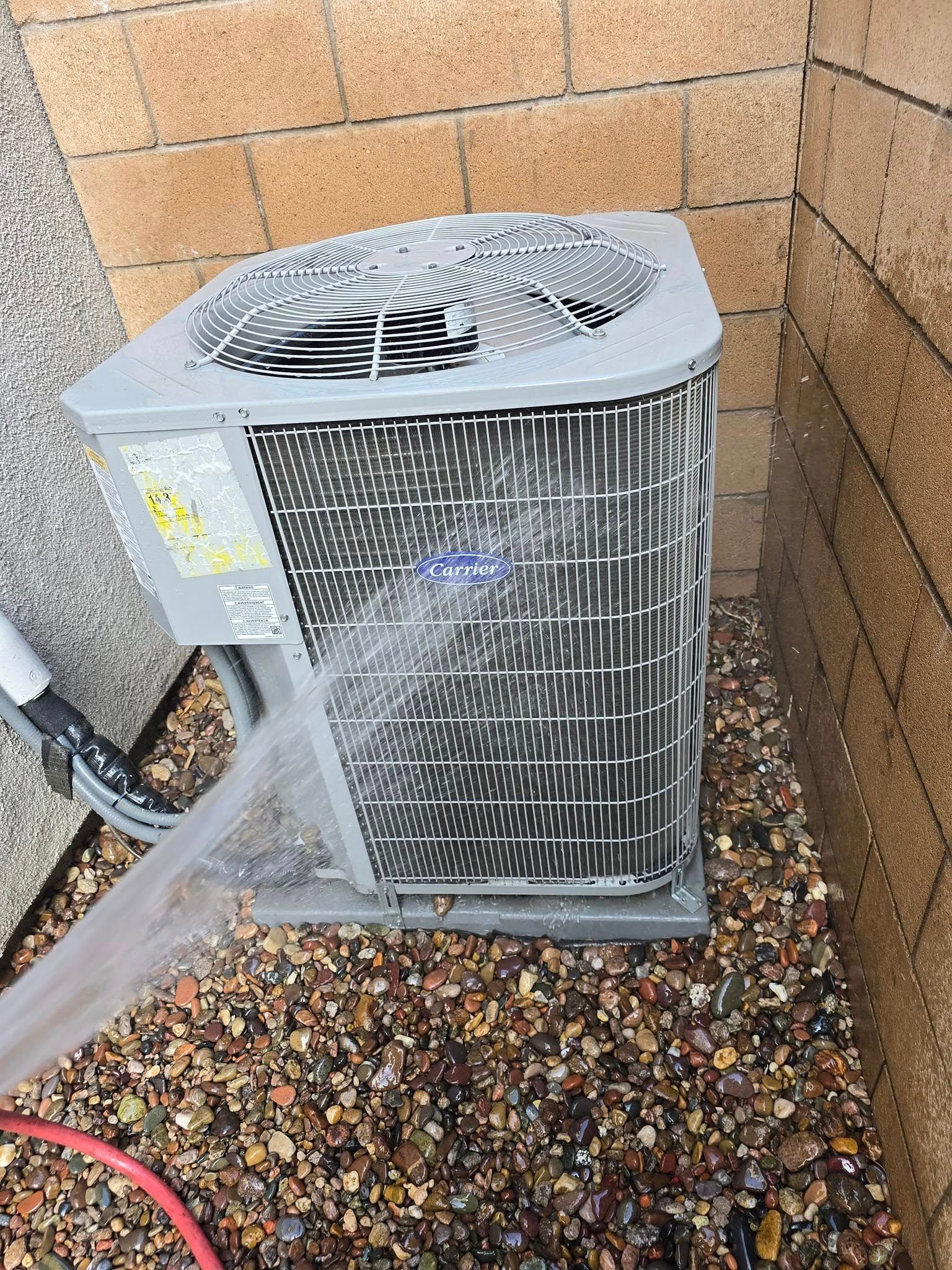 A large air conditioner is sitting on top of a pile of gravel next to a brick wall.
