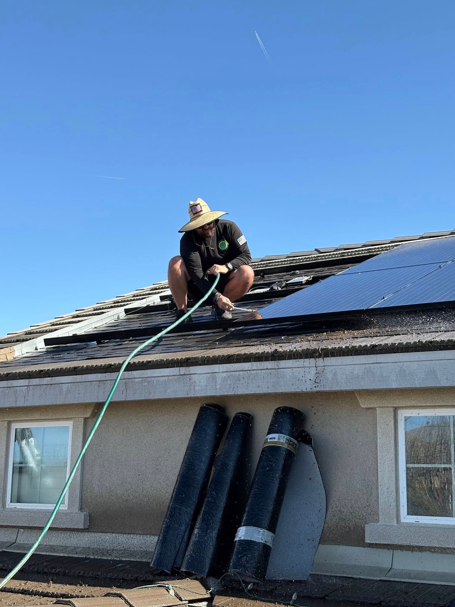 A man is kneeling on the roof of a house with a hose attached to him.