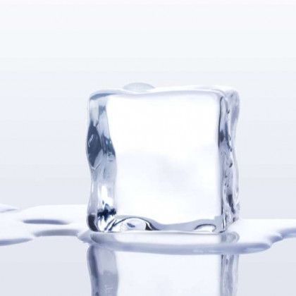 Clear ice cube melting on a reflective surface.