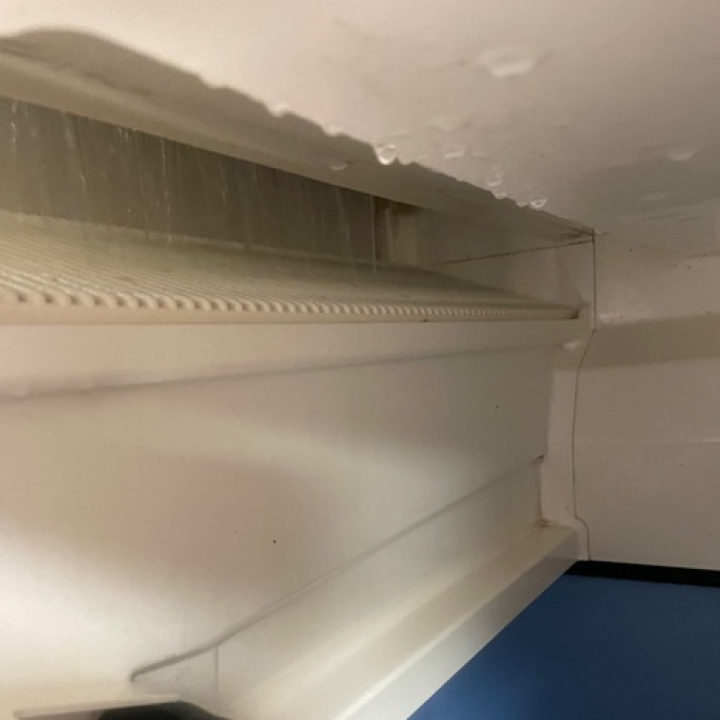Interior of a white refrigerator, heavily iced on the top, with a shelf visible below.