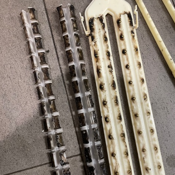 Three dark-stained plastic strips with holes, likely from a printer. Some strips are partially melted.