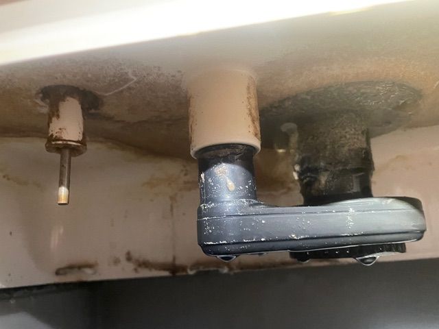 Close-up of a toilet tank interior, showing flush valve assembly and fill valve with water stains.