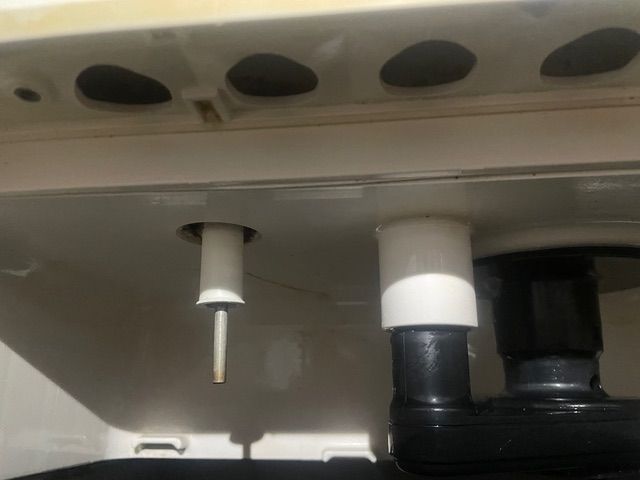Underside of a toilet tank, showing a white fill valve, a flush valve, and the drain pipes.
