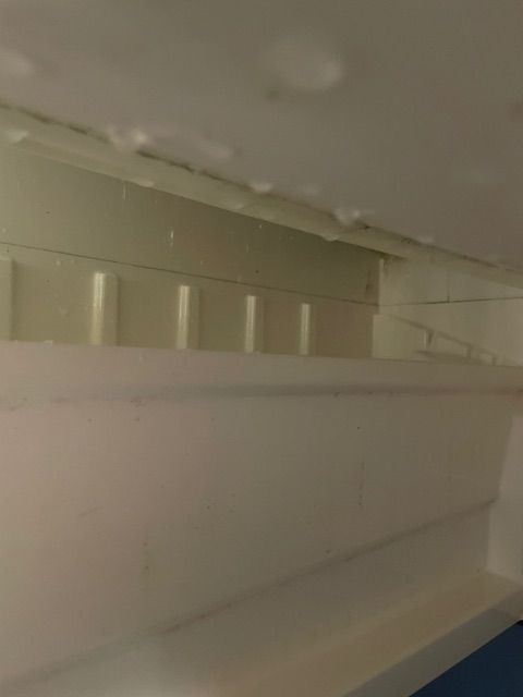 Inside of a white refrigerator, with ice buildup on the top, near the light.