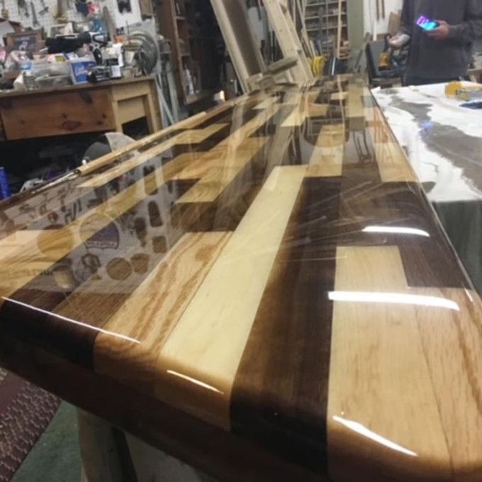 Finished wooden bar top with a glossy epoxy finish. Alternating light and dark wood strips.
