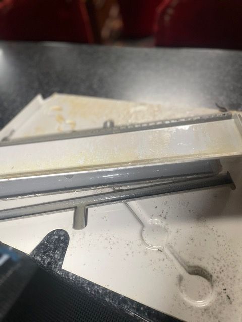 Close-up of a white appliance part, possibly a dishwasher component, with visible dust and residue.