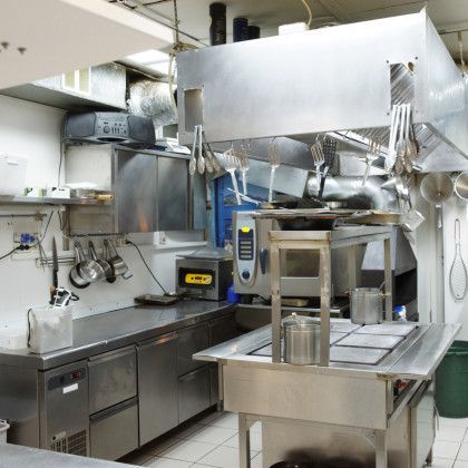 Stainless steel commercial kitchen with appliances and cookware.