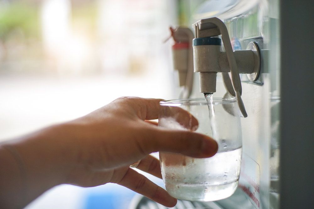 A Person is Pouring Water Into a Glass From a Water Dispenser — Billabong Springs in Jimboomba, QLD