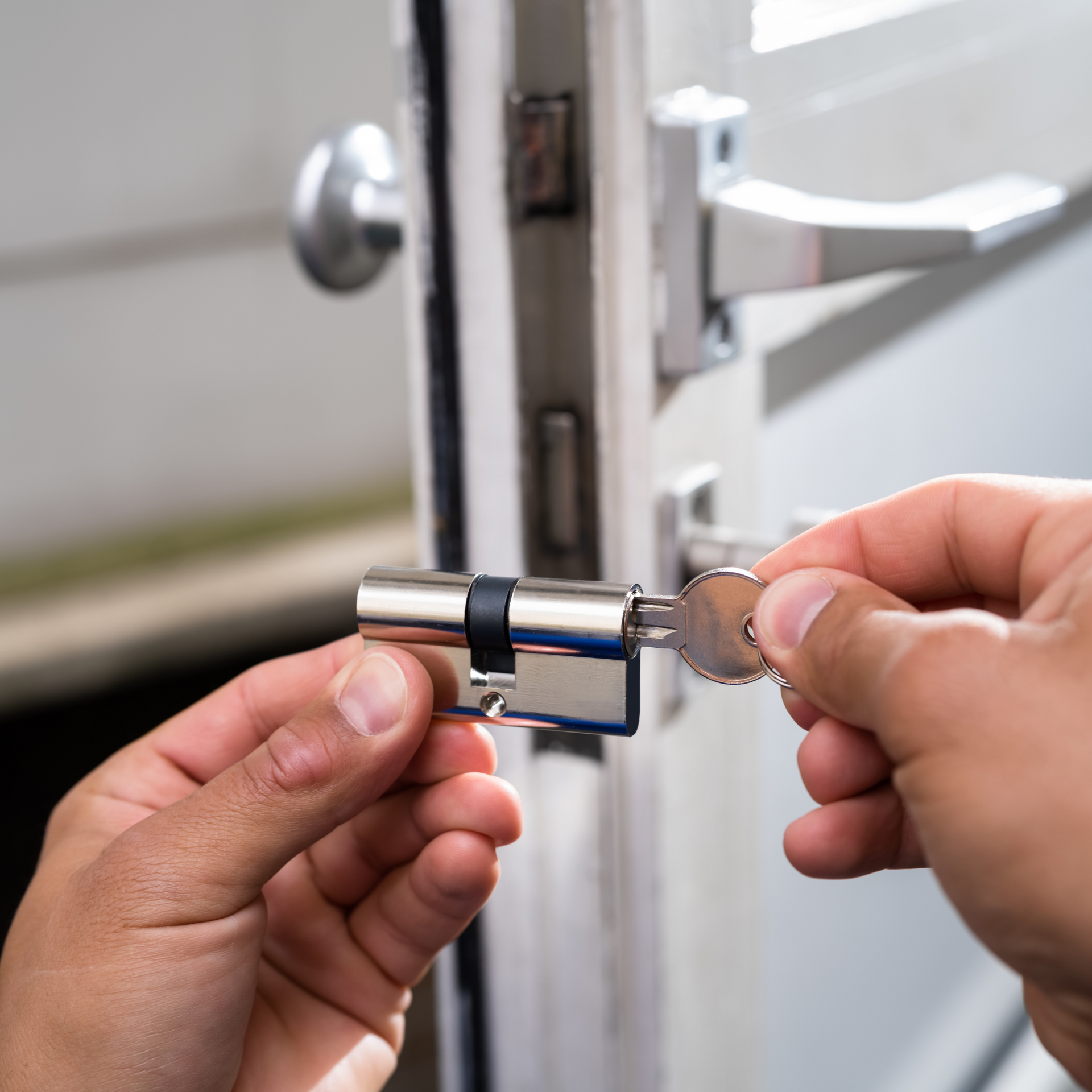 Hands inserting a key into a silver door lock cylinder, installed in a door.