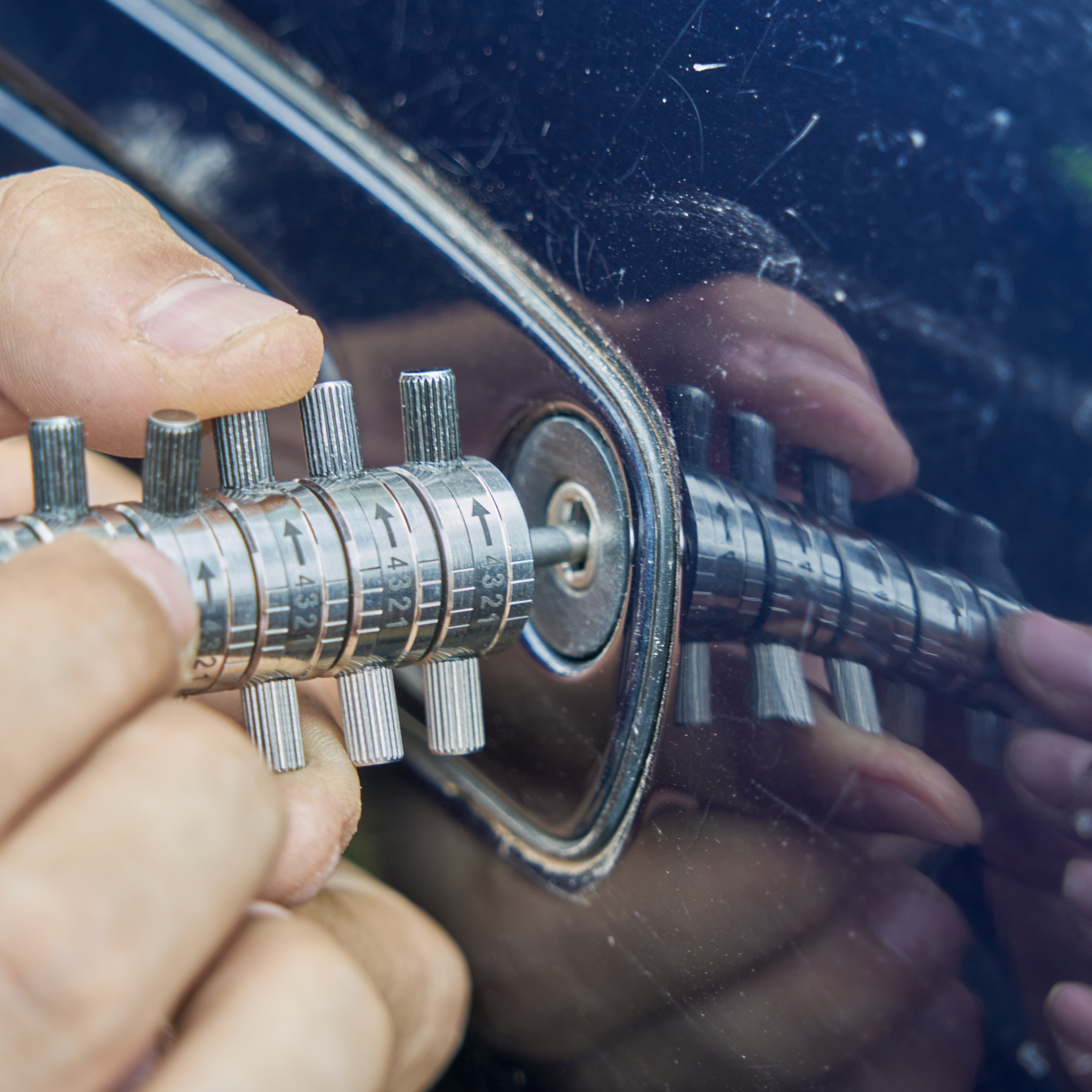 Hands using a lock picking tool to open a car door lock.
