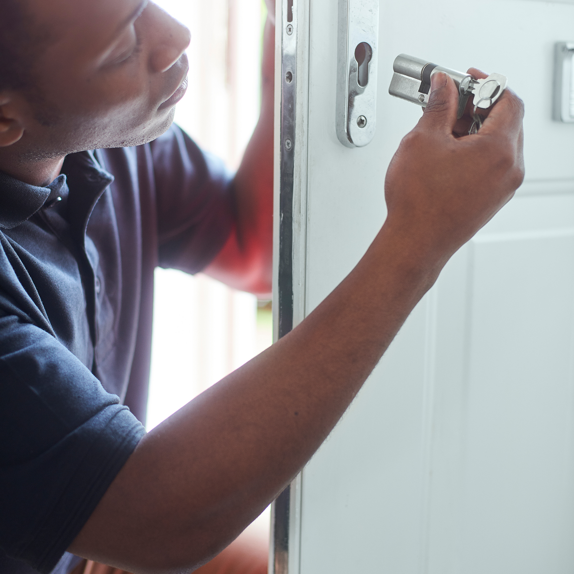 Man installing a door lock. Indoors, white door. Black man, dark skin, focused.