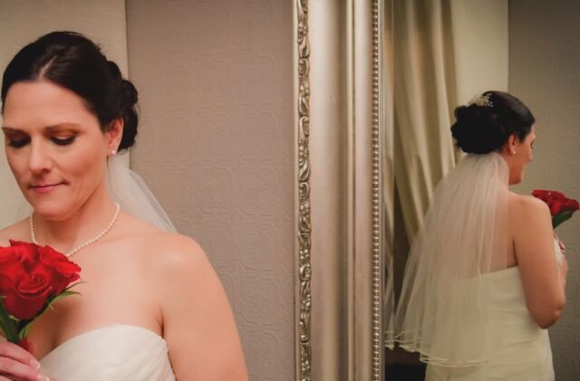 A woman in a wedding dress is holding a bouquet of red roses in front of a mirror.
