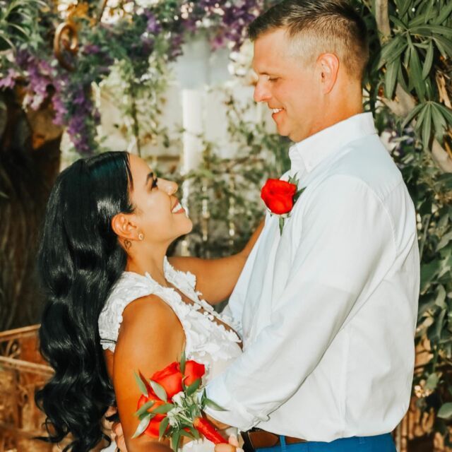 A bride and groom are posing for a picture and the bride is holding a bouquet of red roses