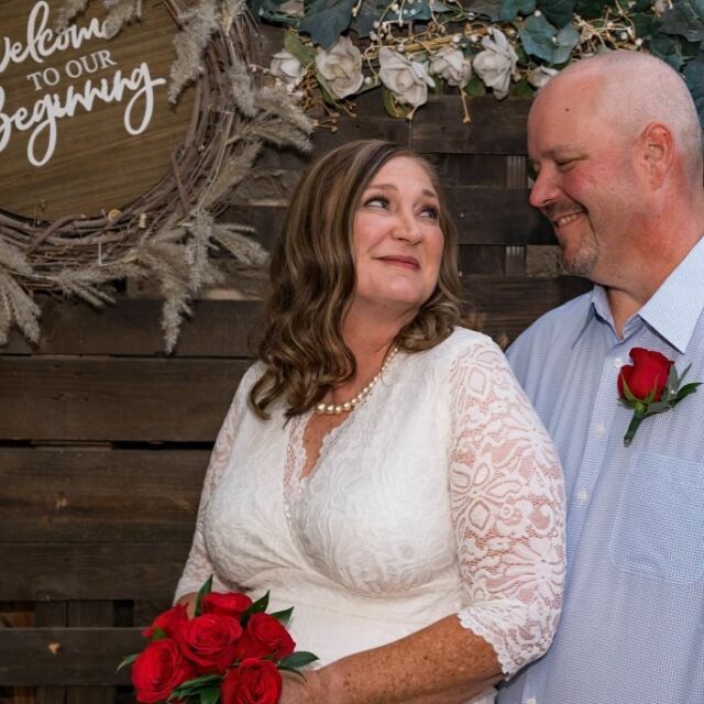 A bride and groom standing in front of a welcome to our beginning sign