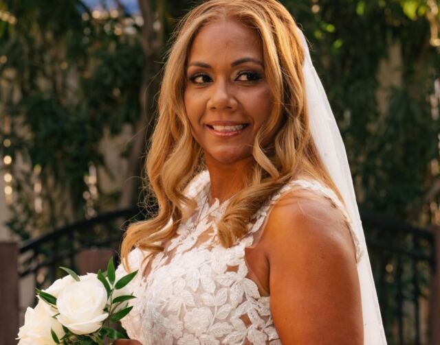 A bride in a white dress and veil is holding a bouquet of white roses.
