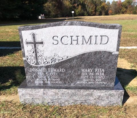 A gray granite headstone for Donald Edward and Mary Rita Schmid, featuring an engraved cross in an outdoor cemetery.