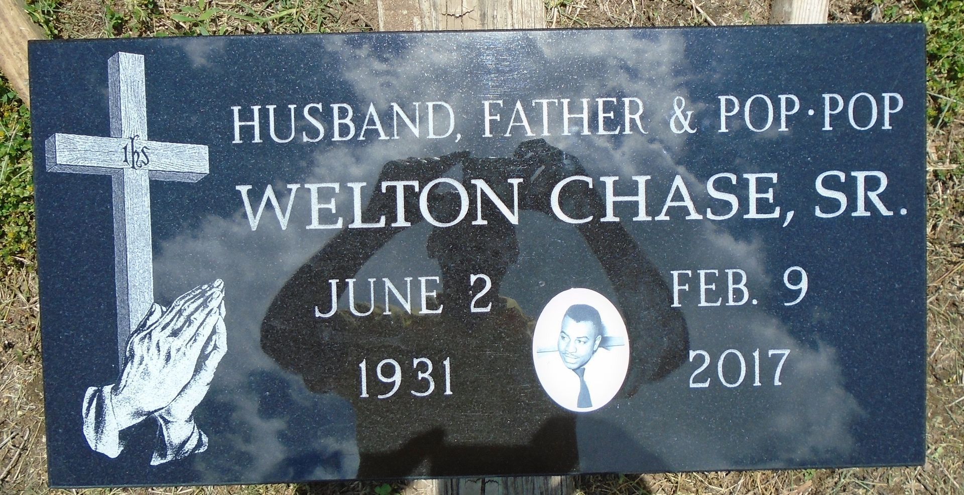 A black granite headstone for Welton Chase, Sr., inscribed with his dates, a cross, praying hands, and a small portrait.