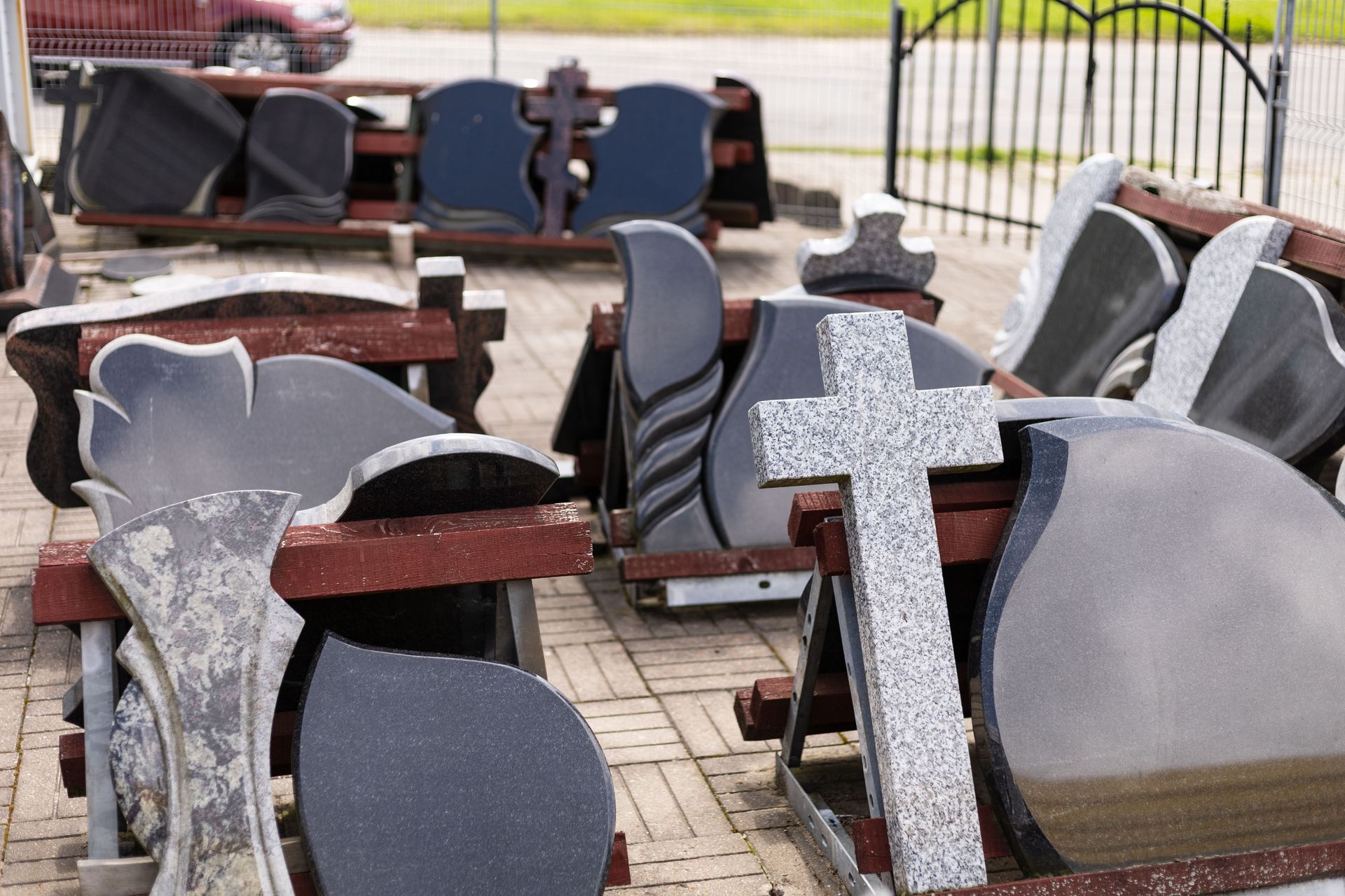 An outdoor display of various polished dark granite headstones and monuments arranged on wooden stands.