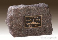 A rough-hewn, dark granite memorial stone with a bronze plaque reading 