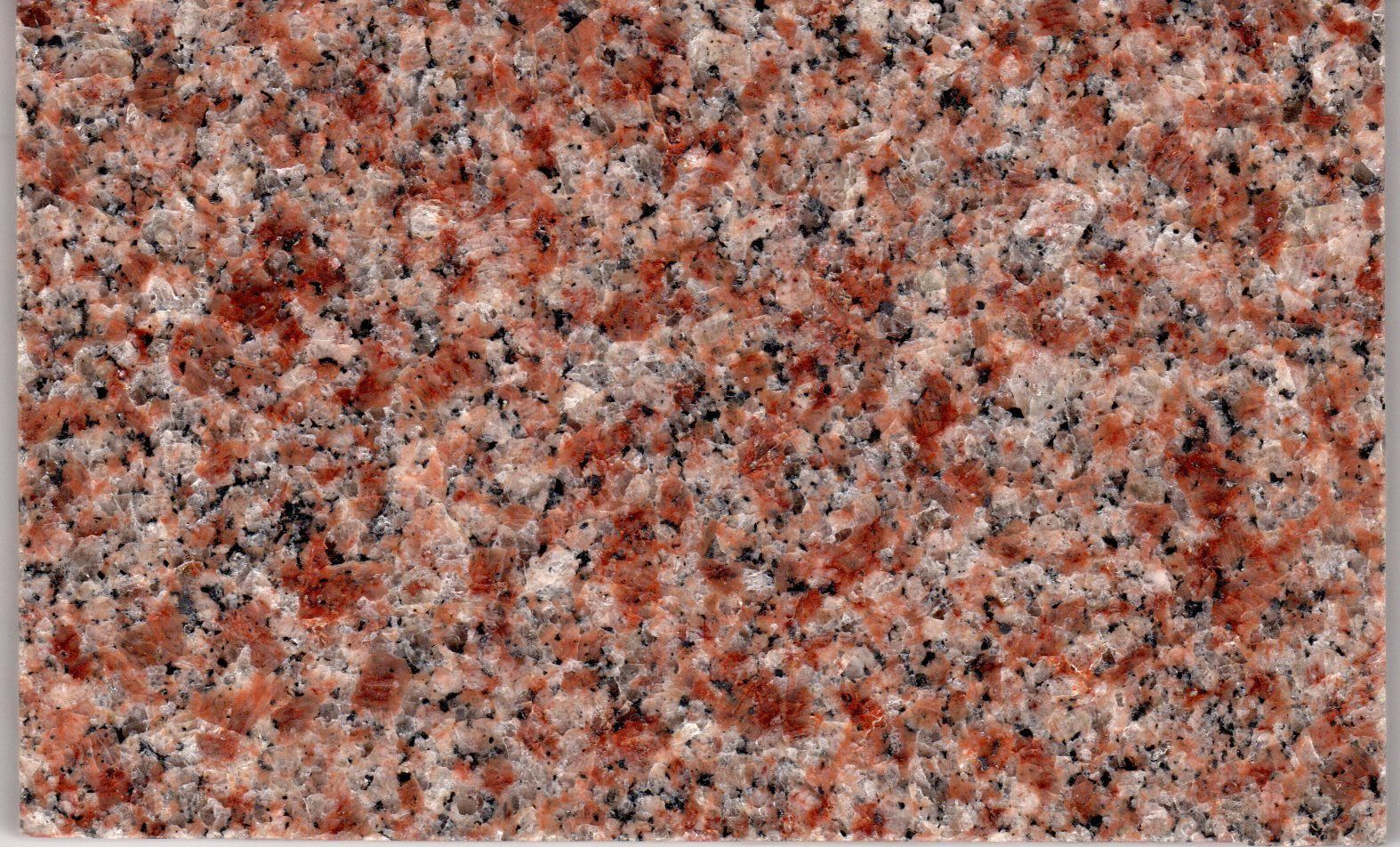 A close-up of a polished granite surface featuring a speckled pattern of reddish-pink, grey, white, and black mineral grains.