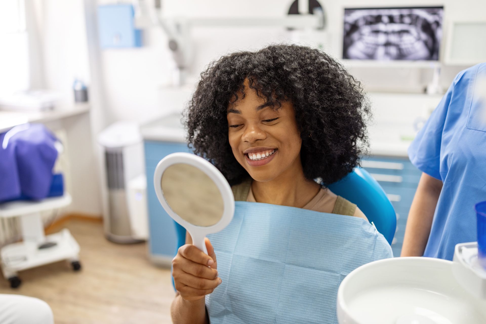 A patient checks her bright smile in a hand-held mirror after a dental session in a clinic.