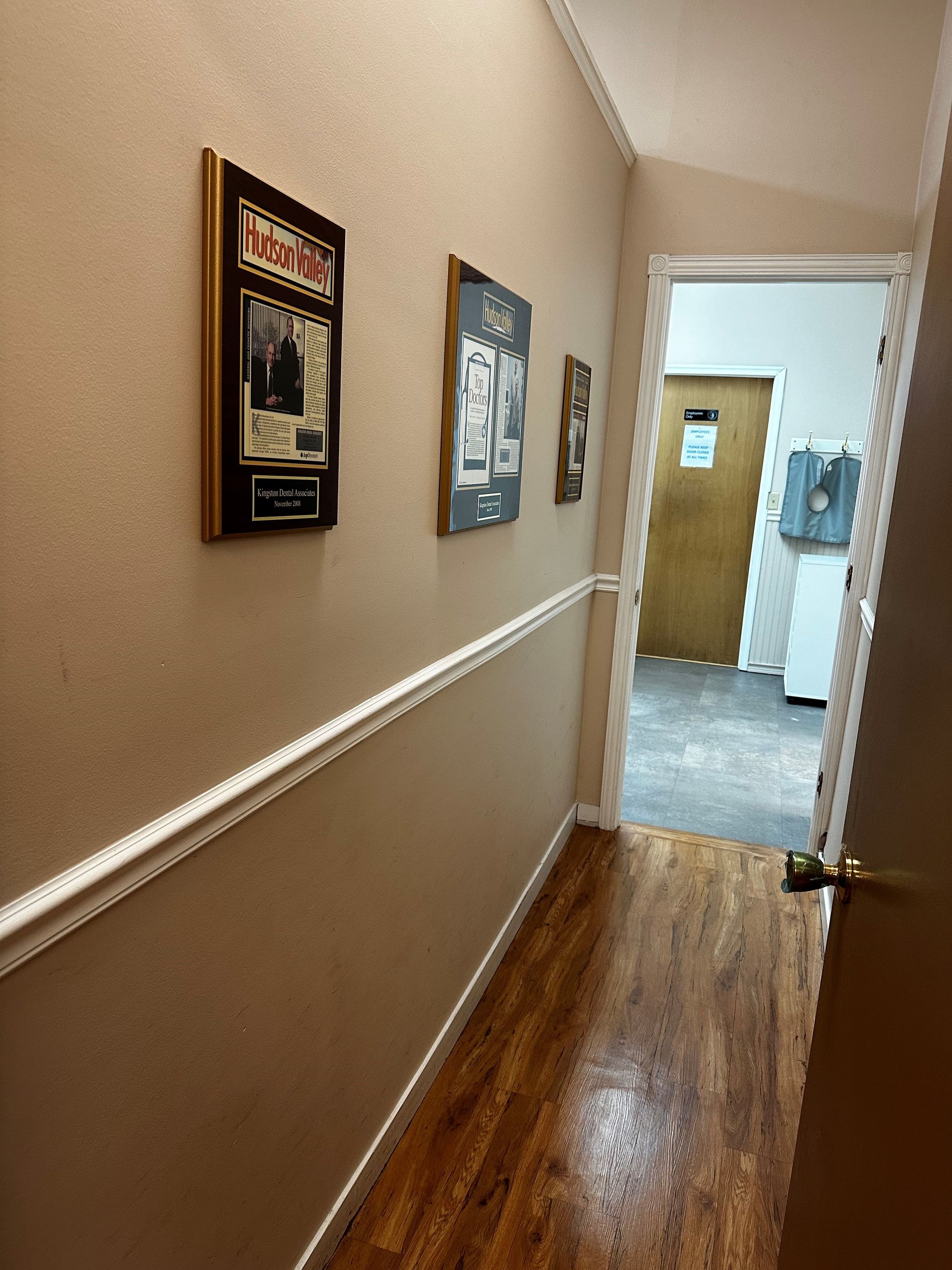 Narrow hallway with wood floor, beige walls, and framed pictures. Door at the end.