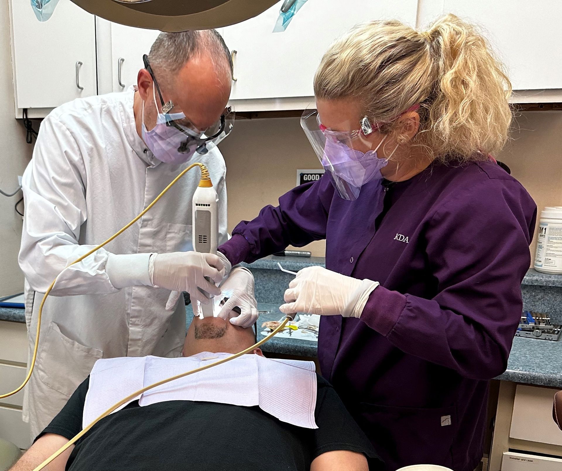 Dentist and assistant working on a patient in a dental office. Both wearing masks, gloves, and protective eyewear.