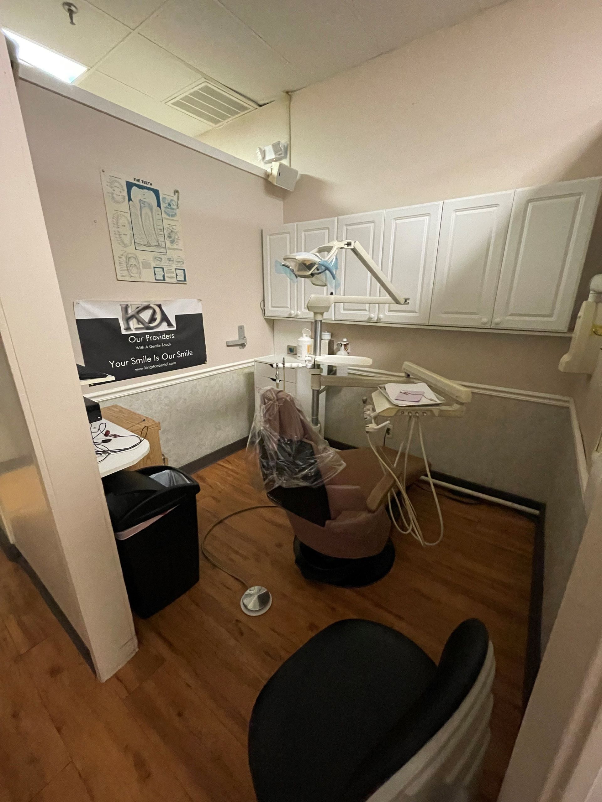 Dental office room with a chair, cabinets, and equipment. Wood floor.