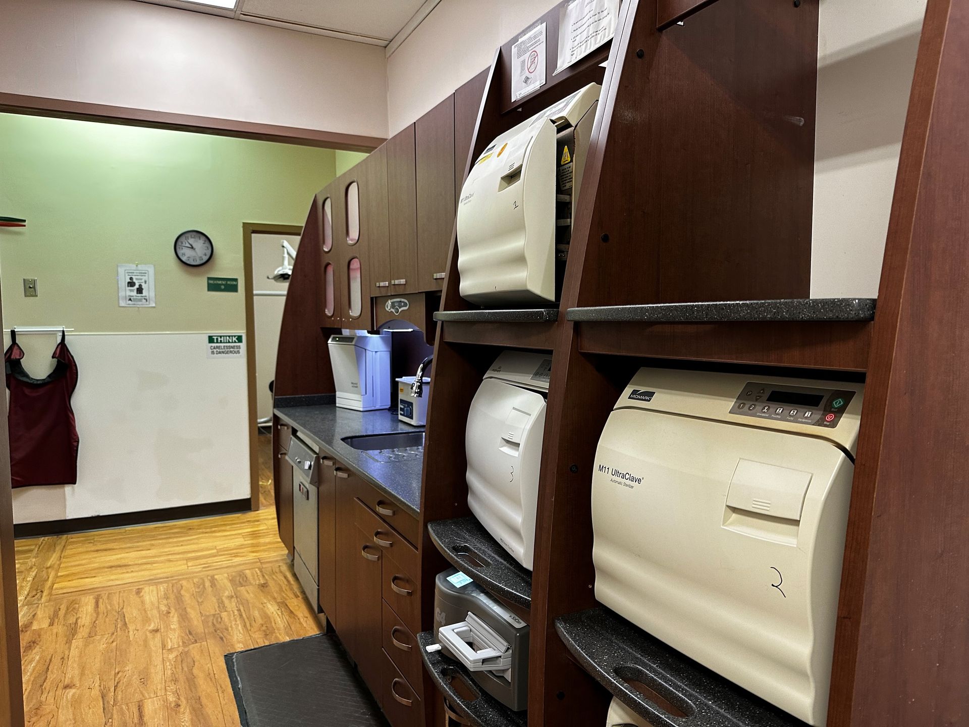 A dental office sterilization area with autoclaves, cabinets, and a doorway to another room.