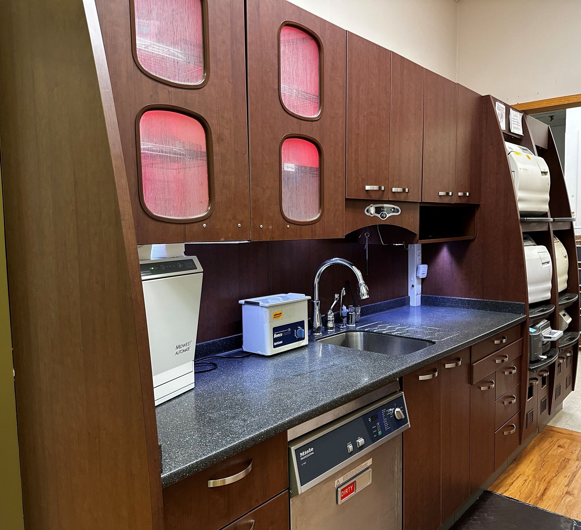 A dental office sterilization area with brown cabinets, sink, and countertop equipment.