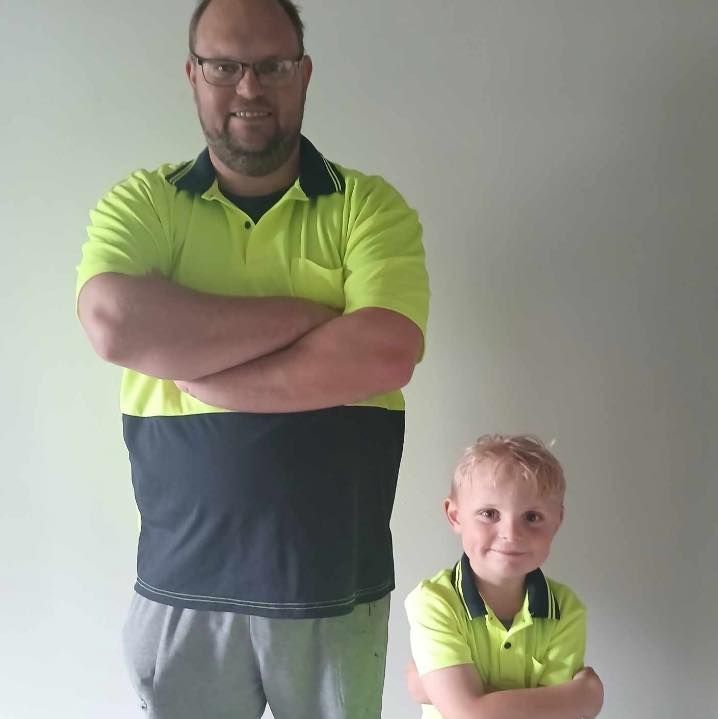 Man and child wearing matching neon yellow and navy shirts, arms crossed, smiling.
