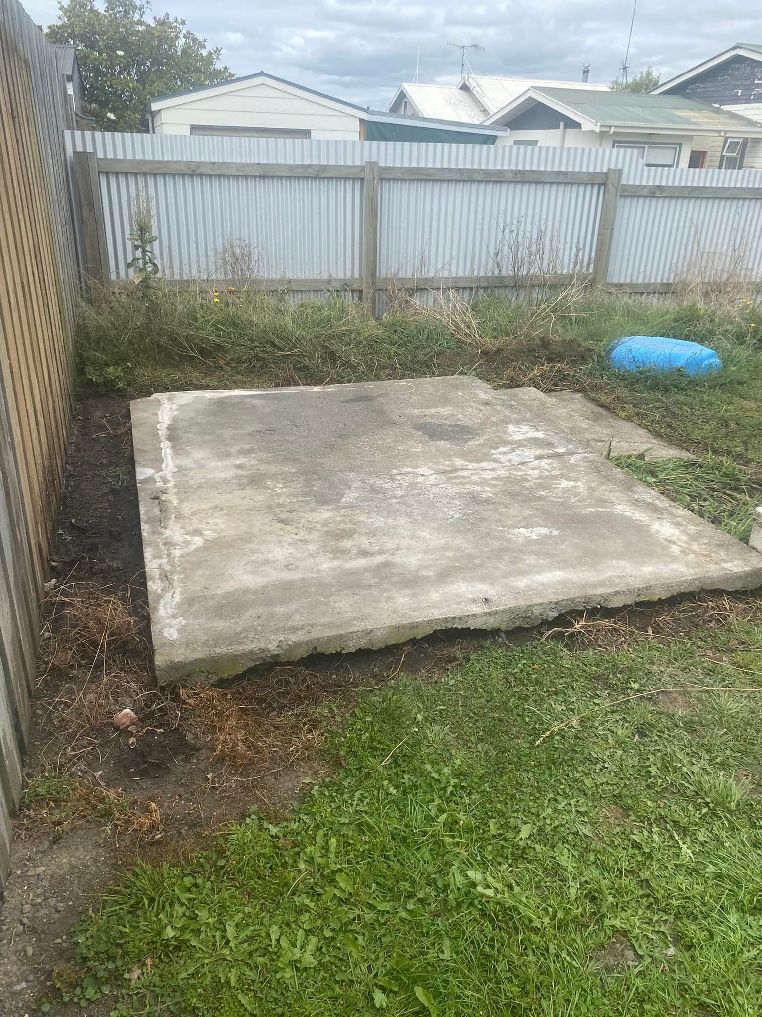 Concrete slab in a grassy yard, near a fence, with houses in the background.