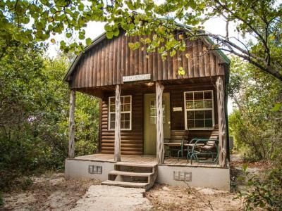 A small log cabin with a porch in the middle of a forest.