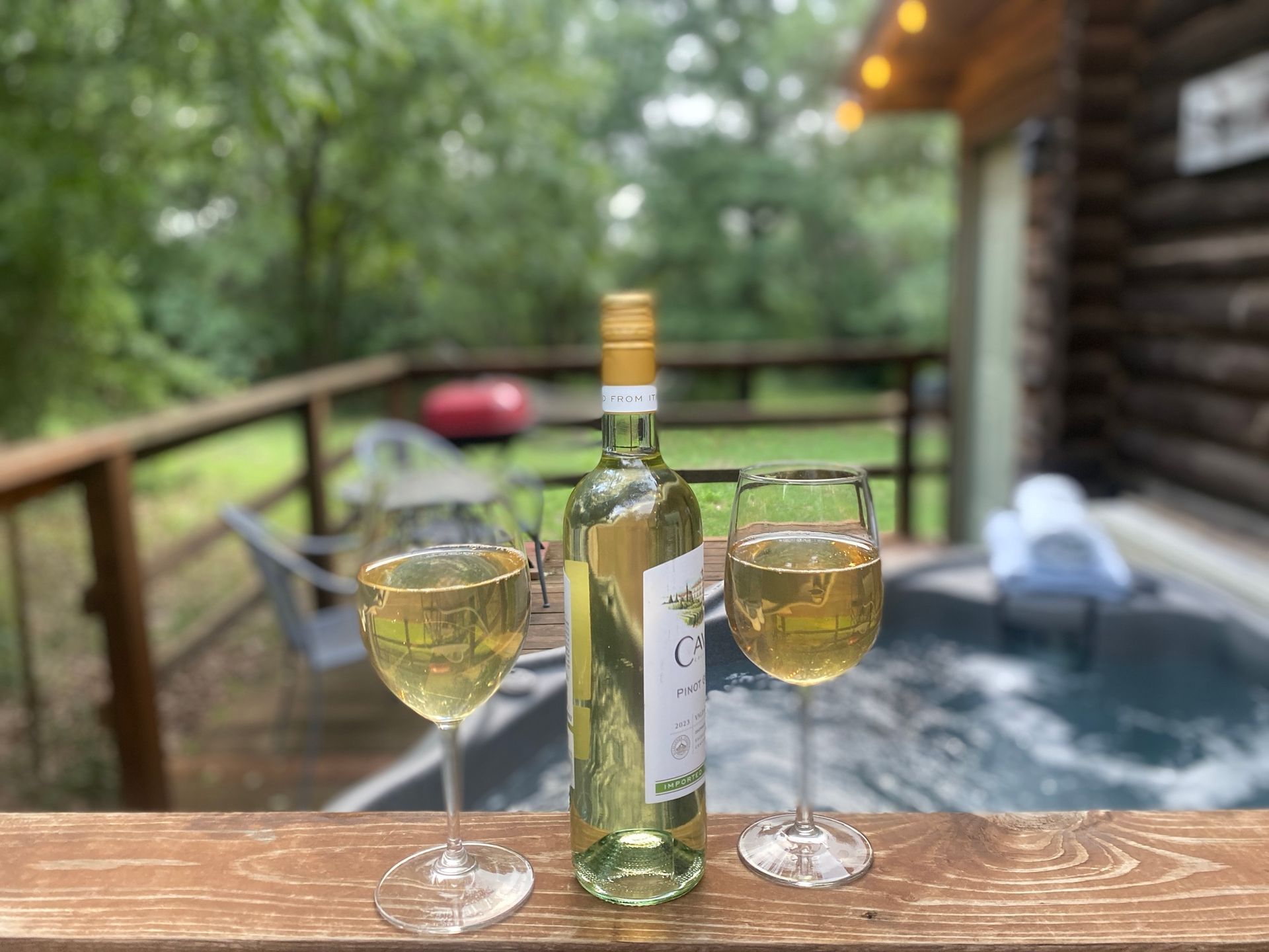 A bottle of wine and two glasses of wine are on a table next to a hot tub.