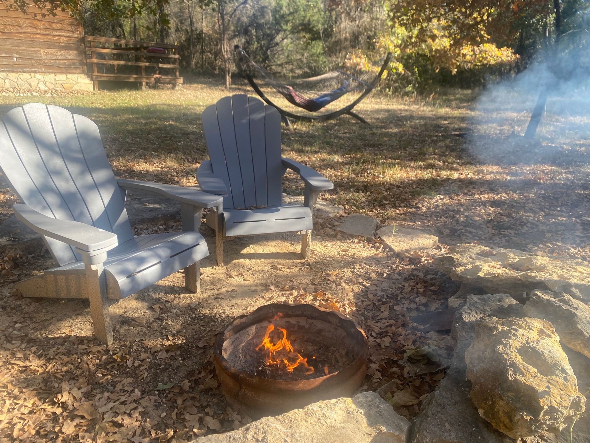A fire pit with two chairs and a hammock in the background.