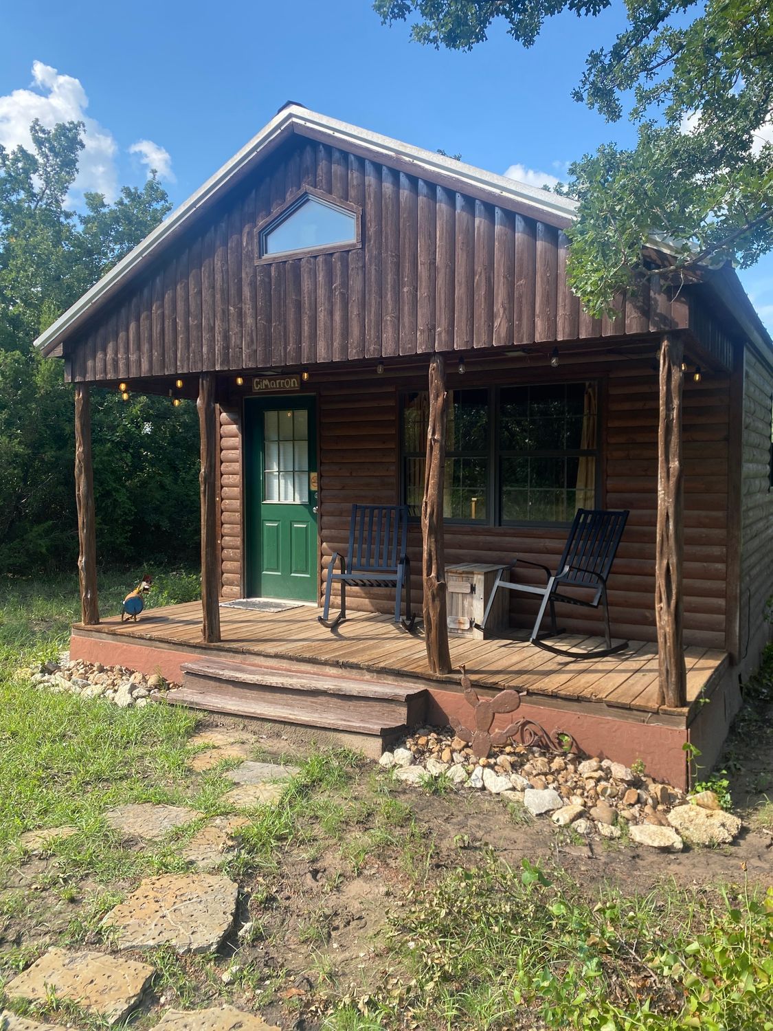 A small log cabin with a porch and rocking chairs on it.
