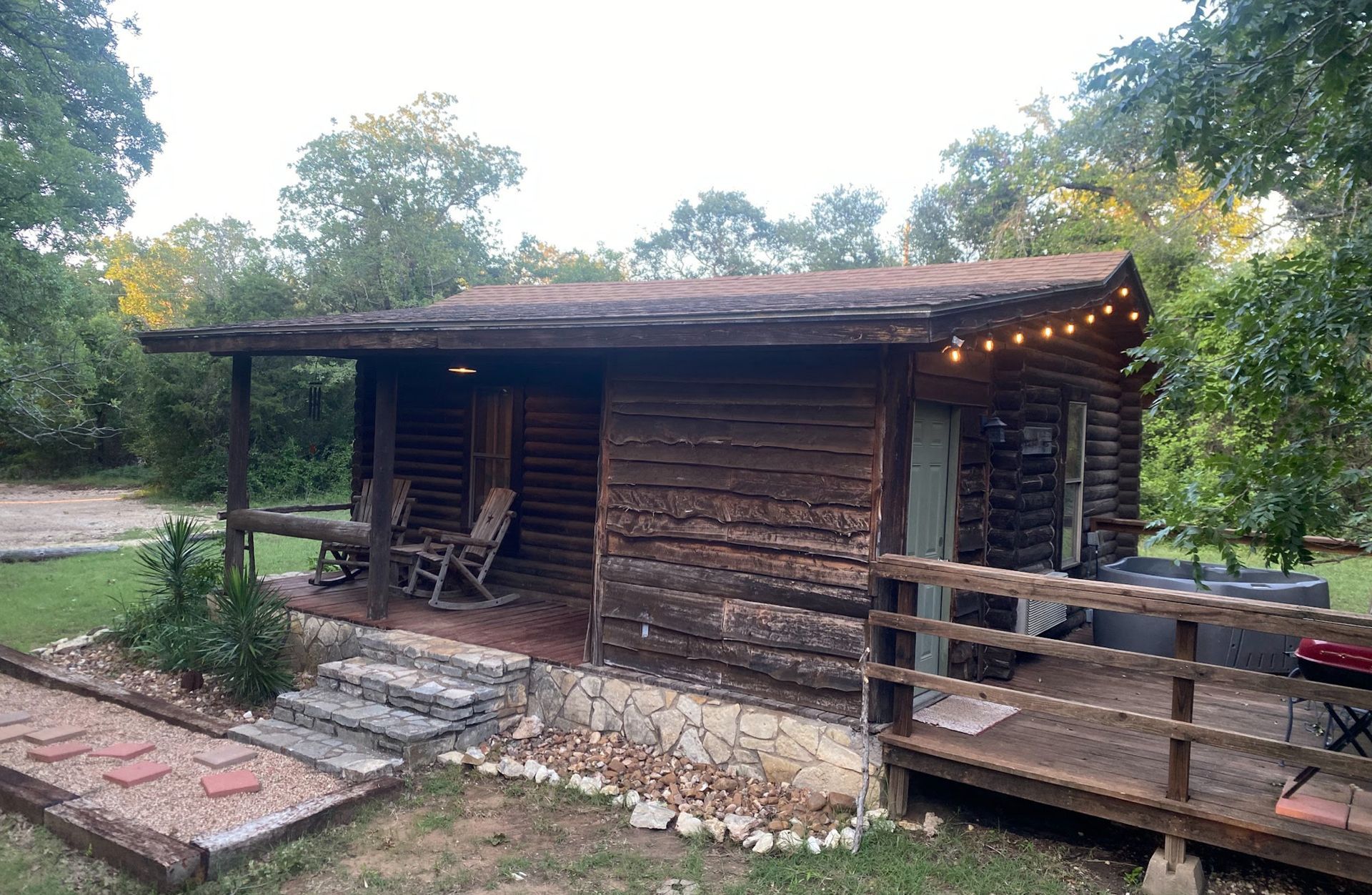A small log cabin with a porch and a hot tub in the backyard.
