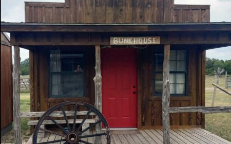 A small wooden building with a red door and a wagon wheel in front of it.