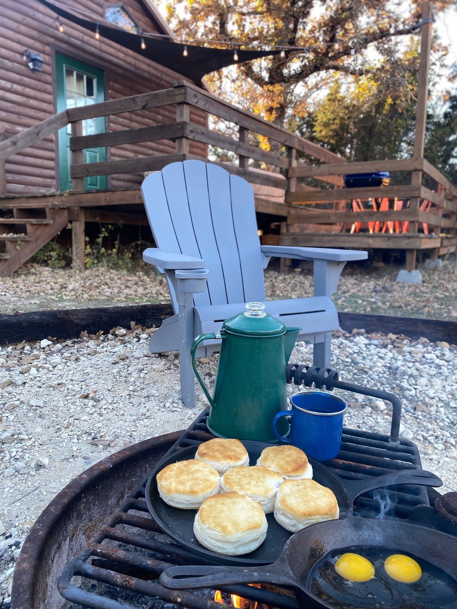 A fire pit with biscuits and eggs on it in front of a cabin.