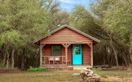 A small red cabin with a blue door and porch in the middle of a forest.
